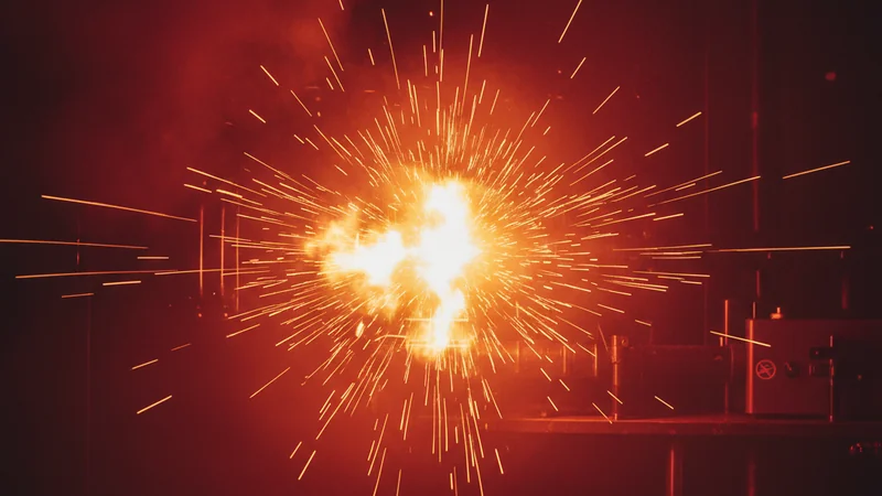 Gold muzzle flash with orange sparks on dark burgundy tactical background